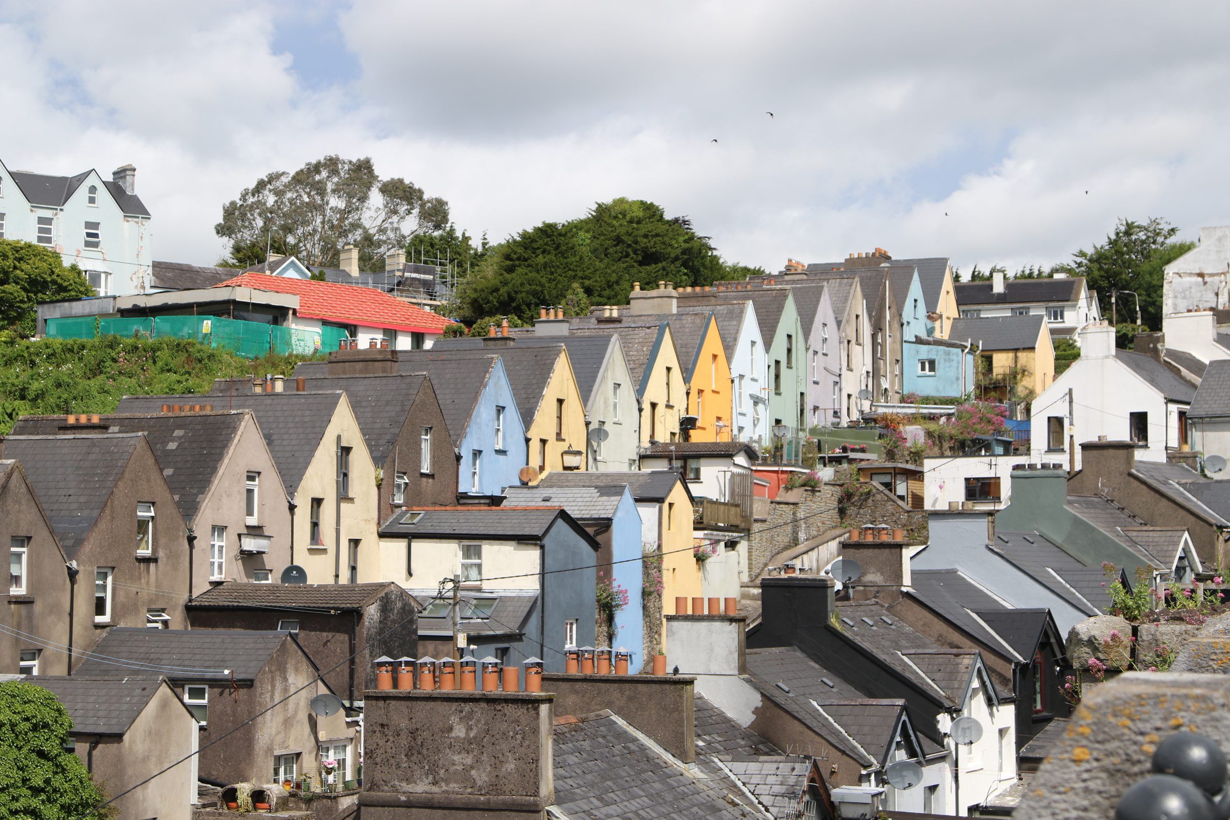 A wide view of pastel gabled houses climbing a hillside among slate roofs and chimney pots under a cloudy sky