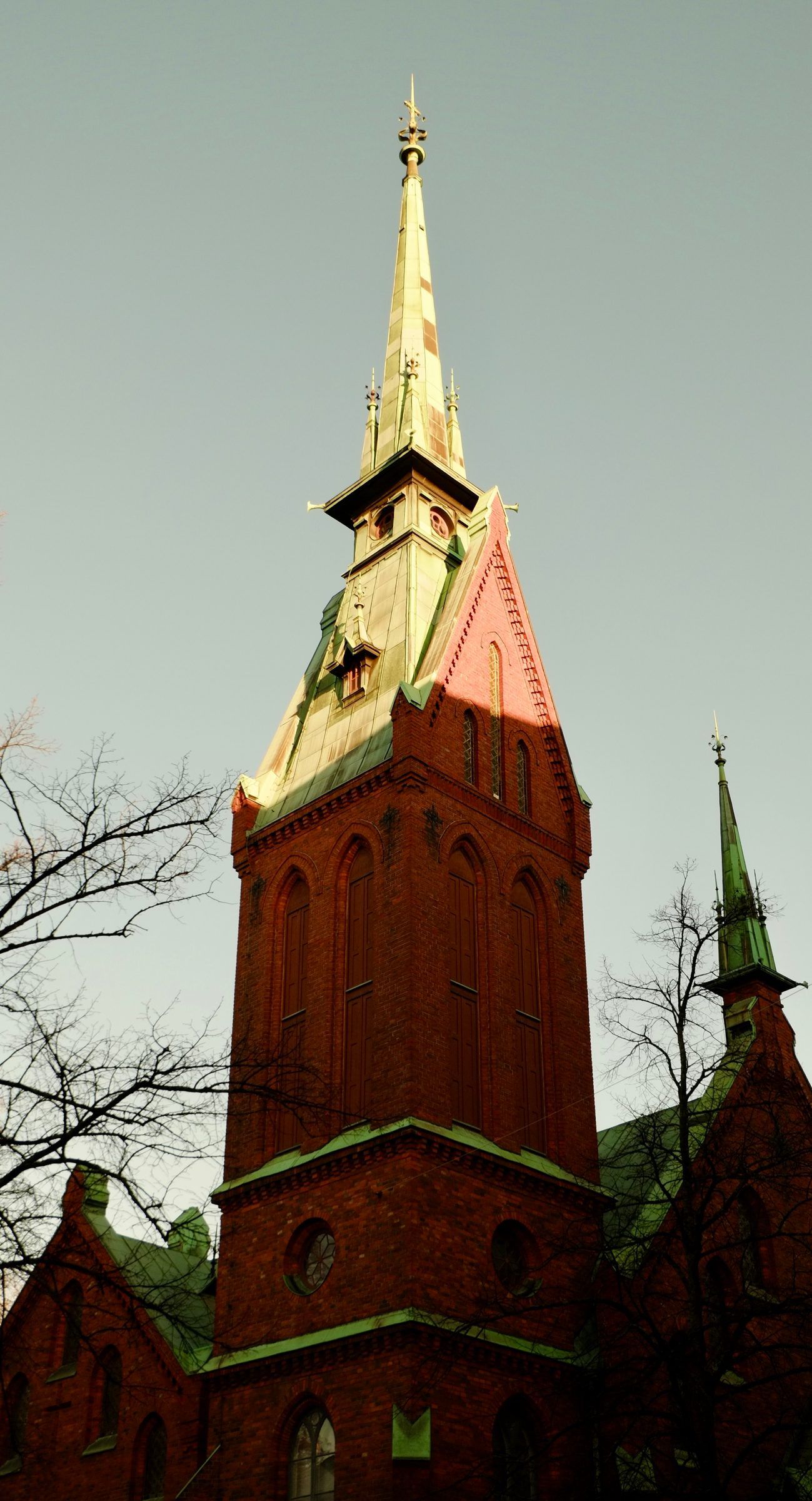 Looking up at a red-brick church tower with a green and gold copper spire catching the light
