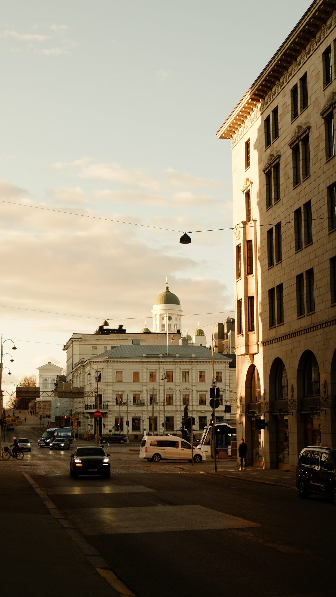 A quiet street in low evening light with pale stone buildings, a green cathedral dome at its far end