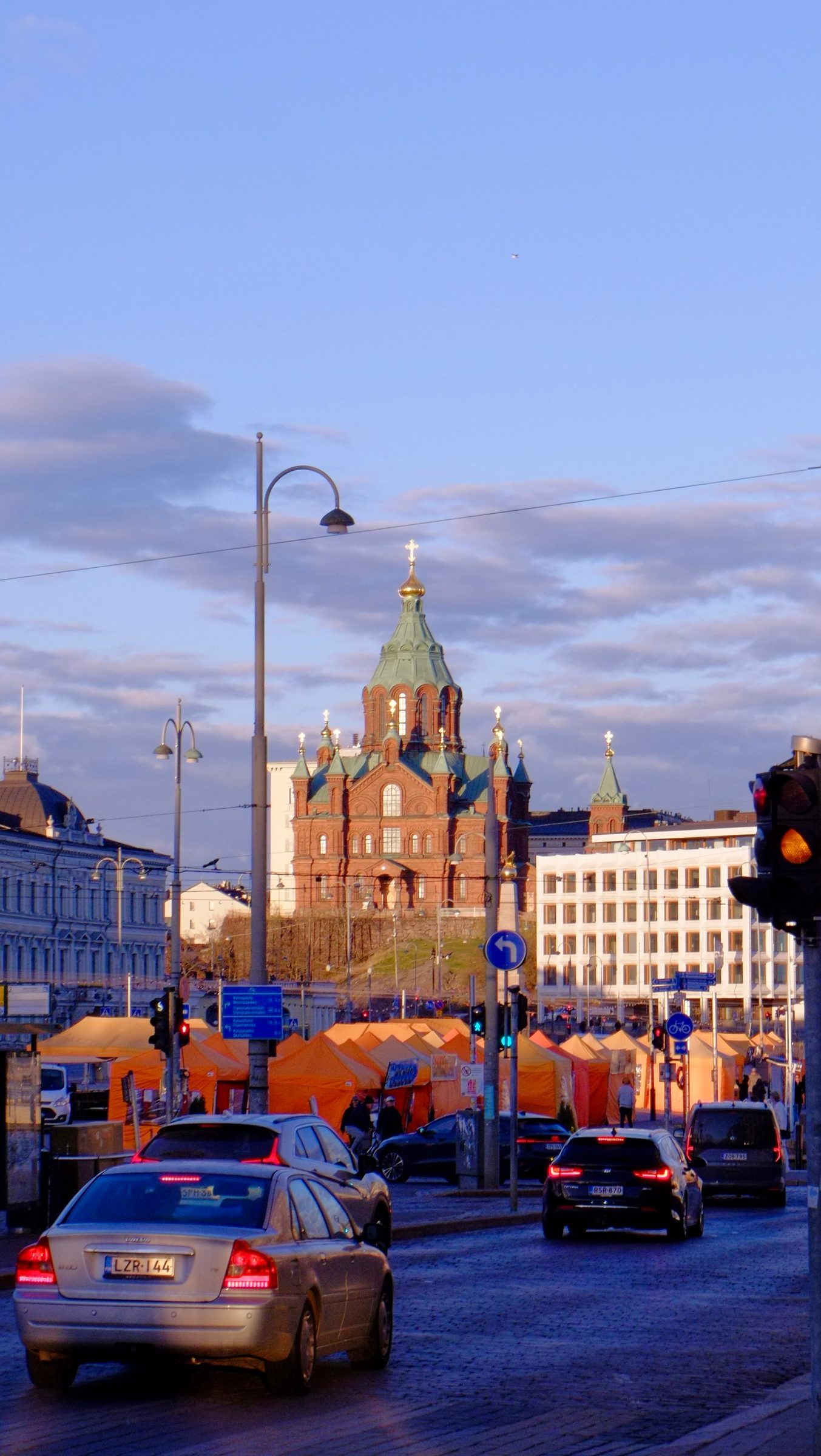 Cars waiting at lights beside orange market tents, the red-brick Uspenski Cathedral rising on its hill behind