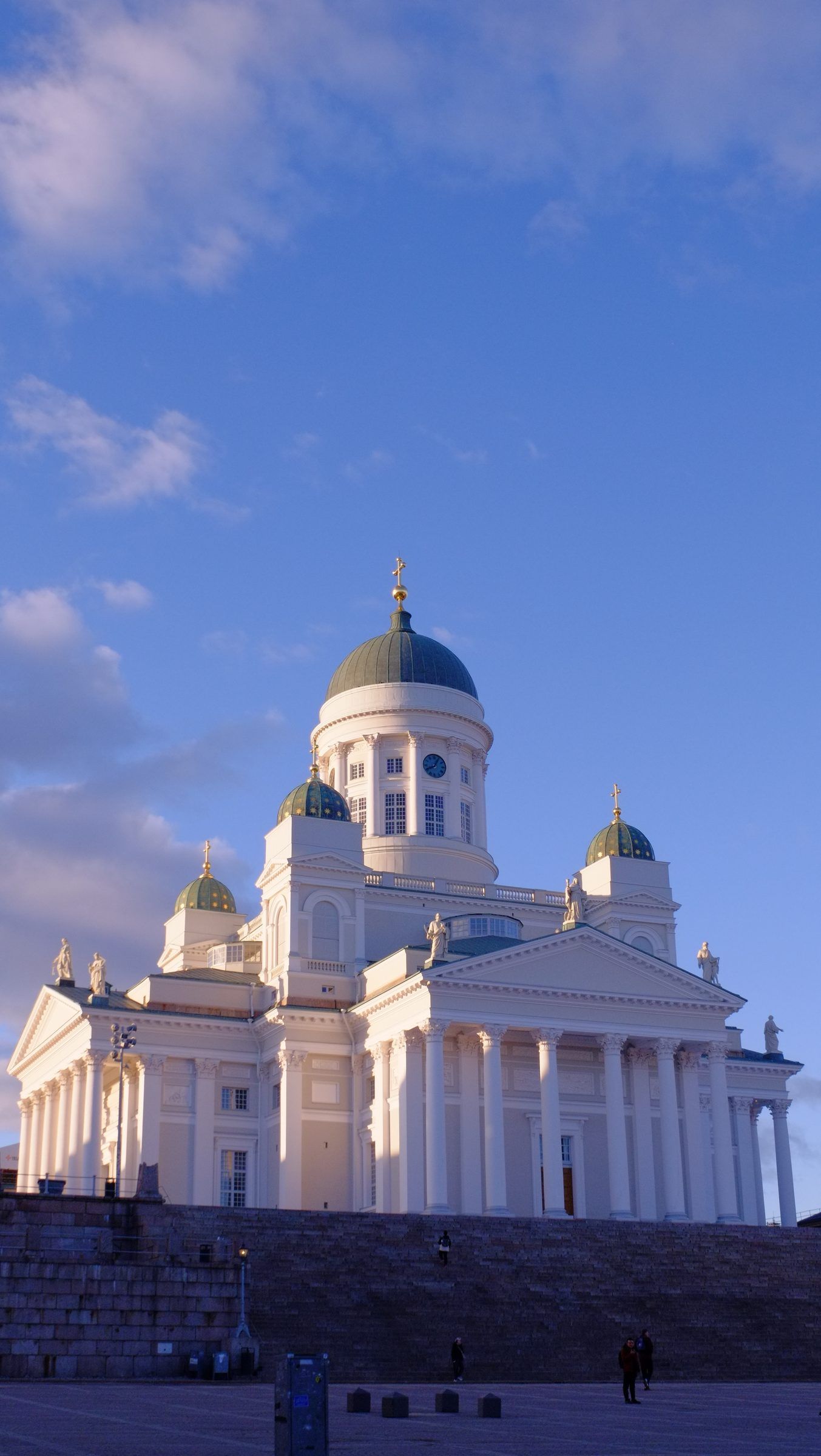 The white neoclassical cathedral with green domes at the top of its broad stone steps under a blue sky