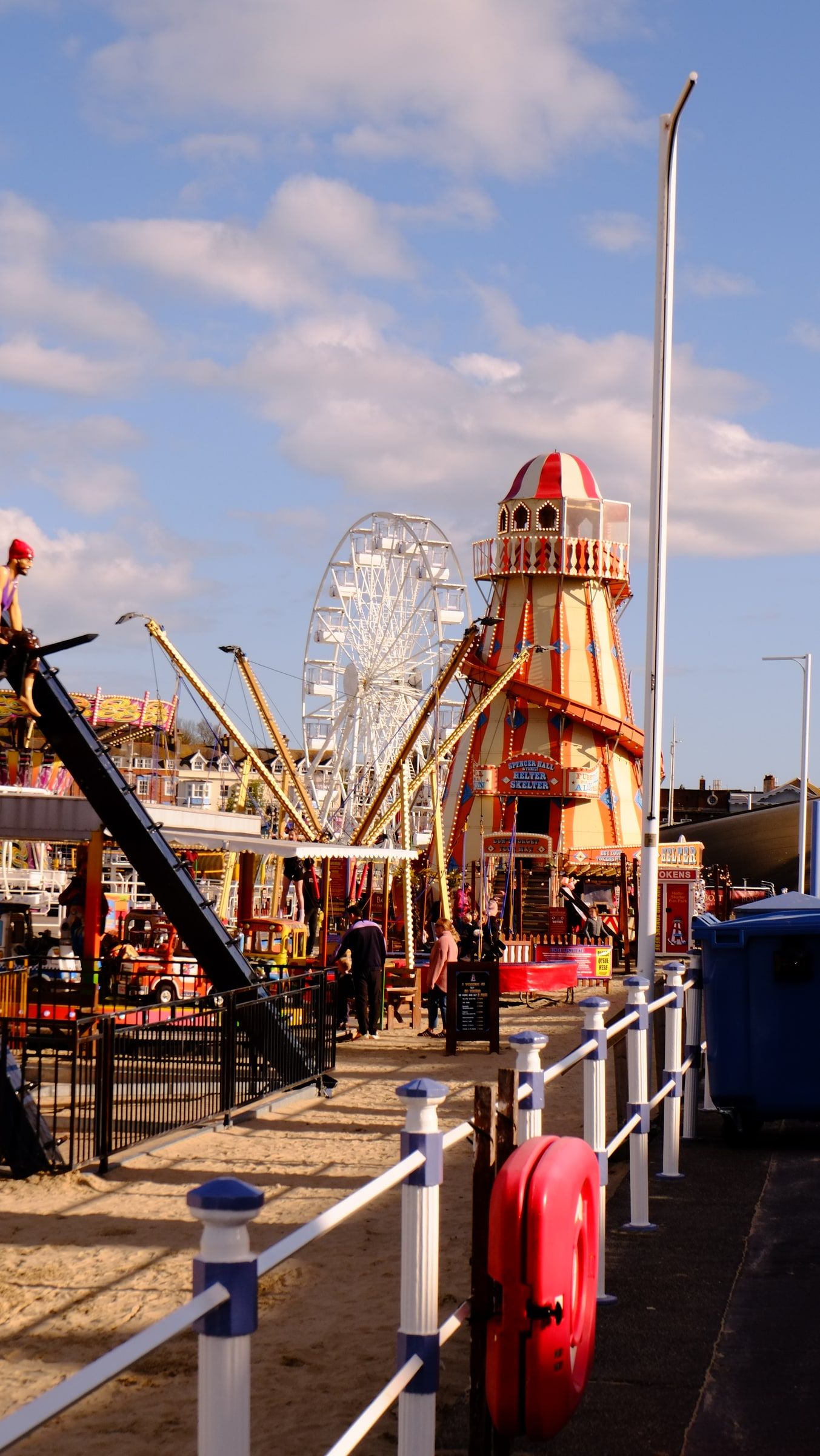 A striped helter-skelter and a Ferris wheel on Weymouth seafront, beside a white railing and a red lifebuoy