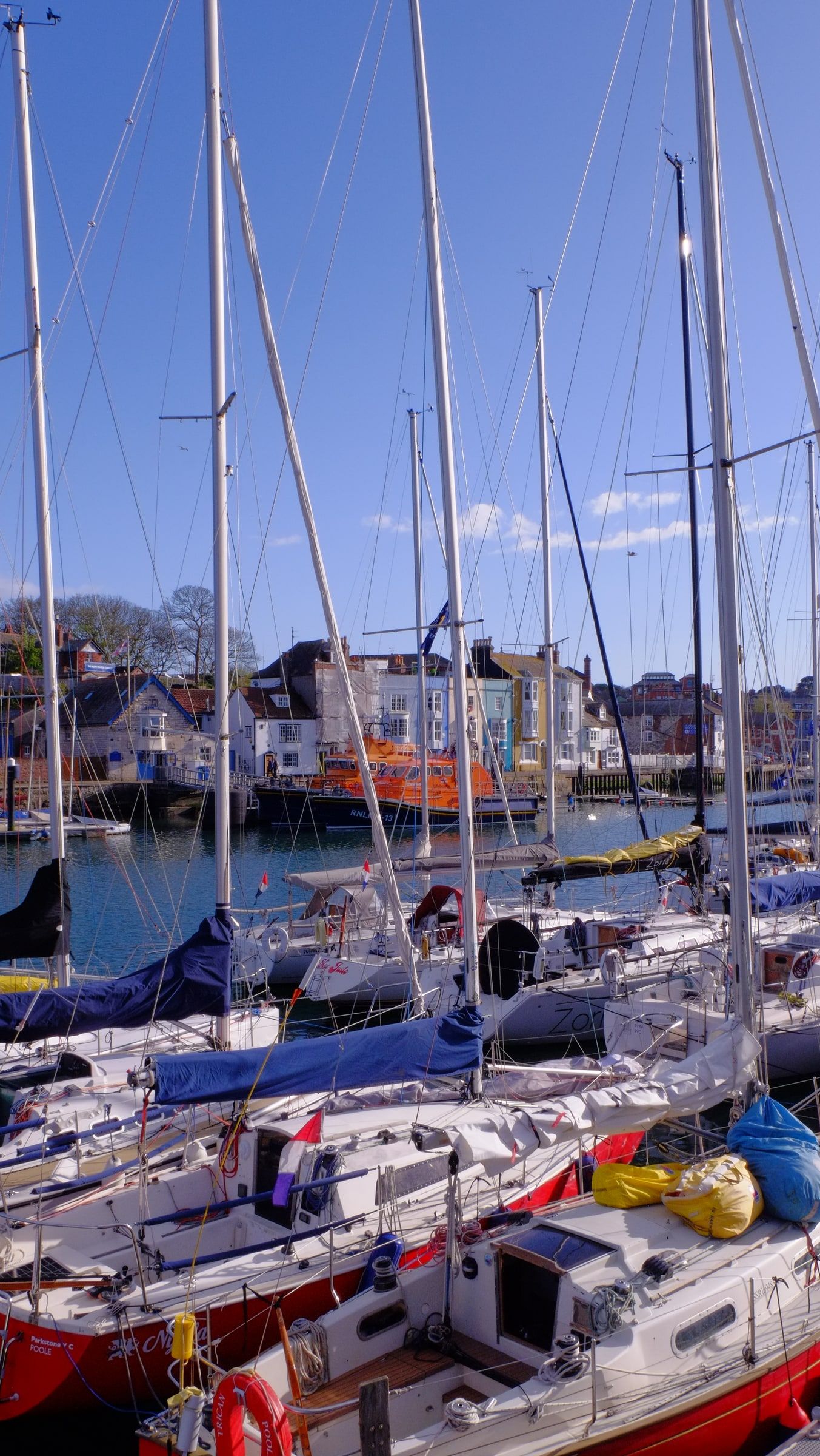 Rows of moored sailing yachts with tall masts in Weymouth harbour under a clear blue sky
