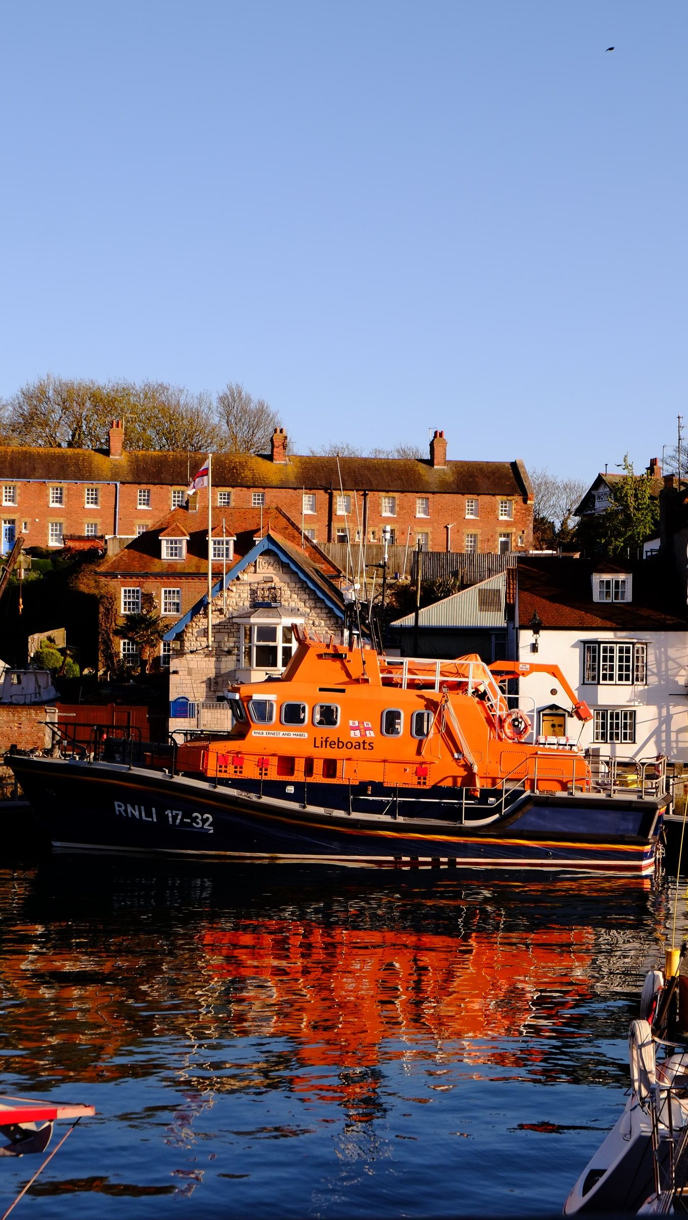 The orange RNLI lifeboat moored in front of brick terraces, its colours reflected in the harbour