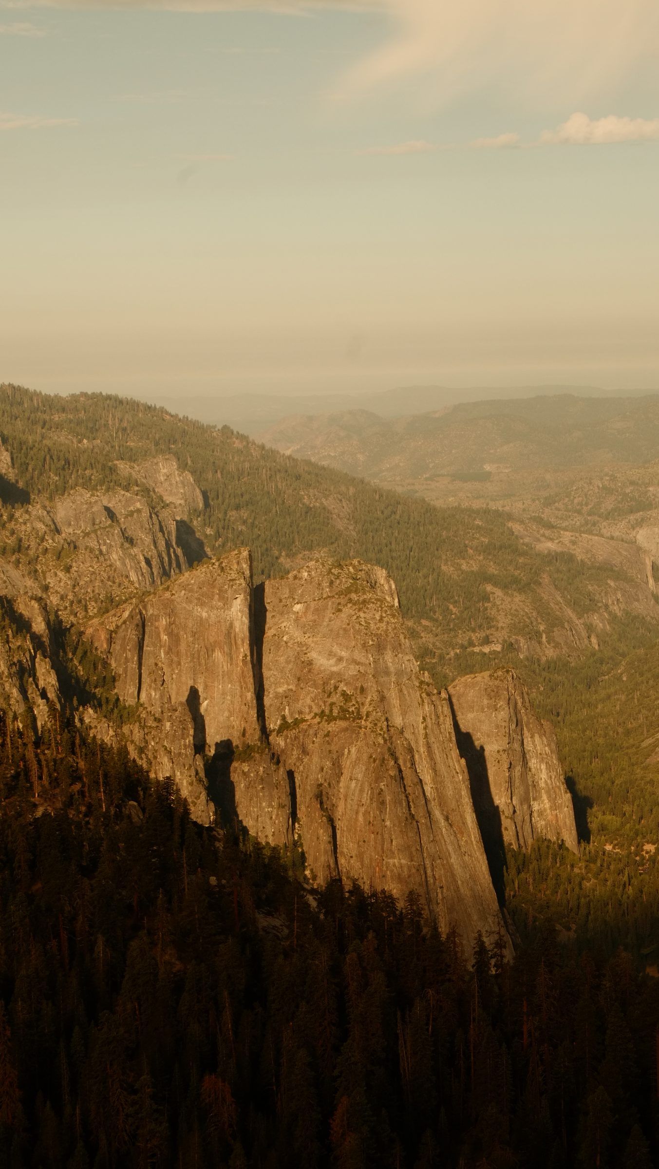 Jagged granite spires catching warm low sun above a dark pine forest, hazy foothills beyond