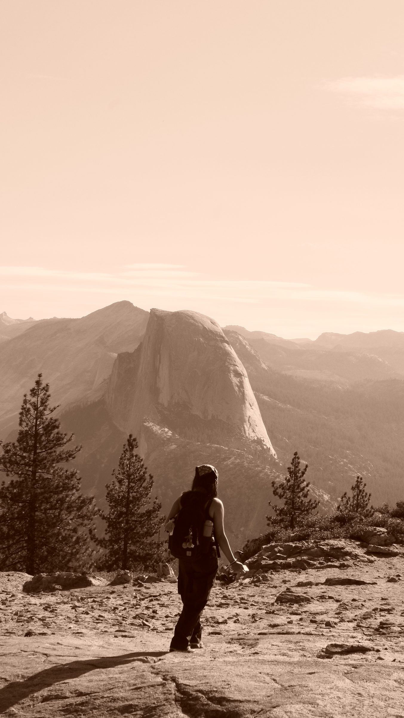 A sepia view of a hiker with a backpack walking across bare granite toward Half Dome